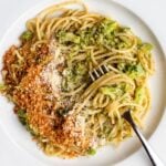 White plate with spaghetti in a broccoli sauce and toasted panko crumbs on top. Fork rests in.