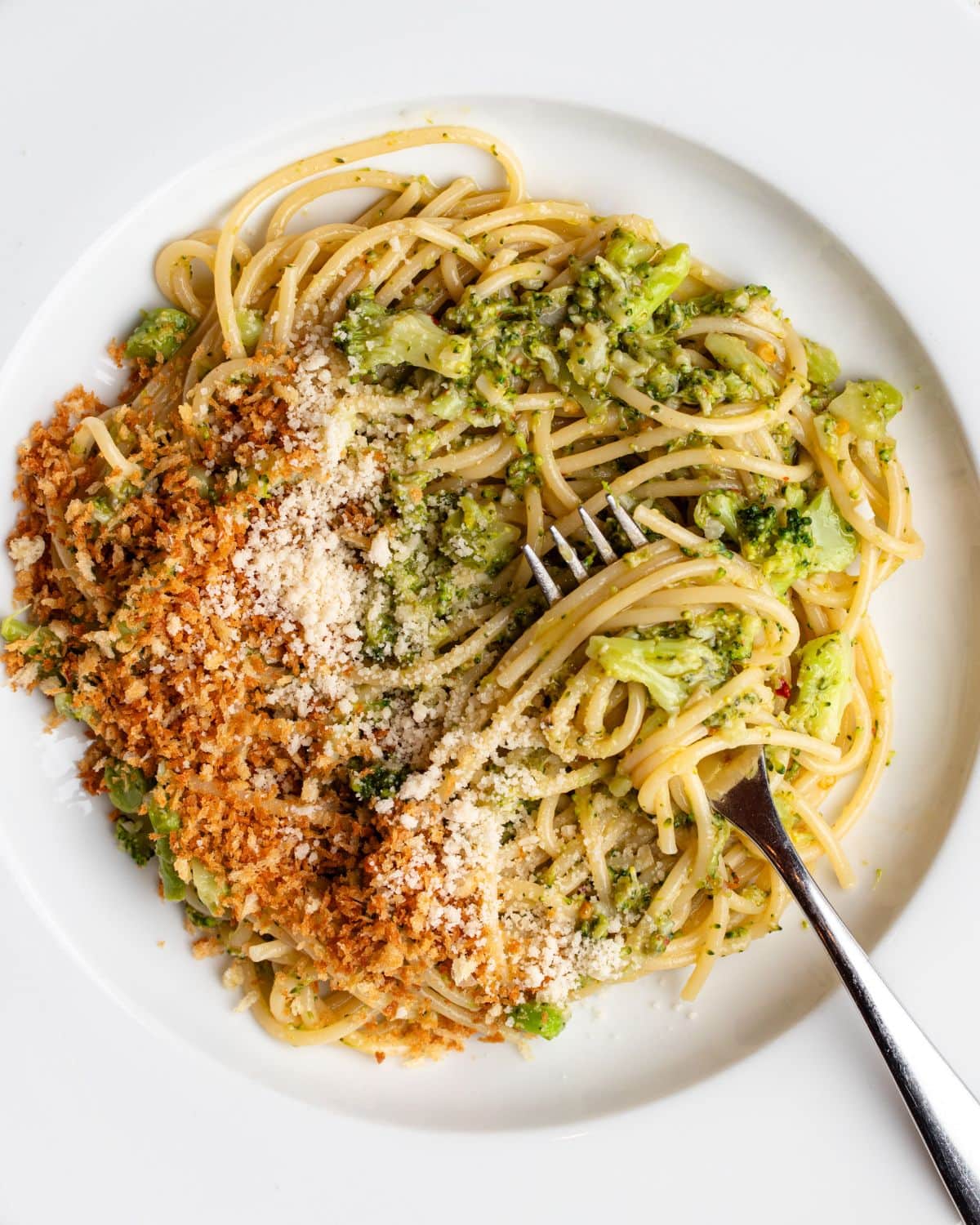 White plate with spaghetti in a broccoli sauce and toasted panko crumbs on top. Fork rests in.