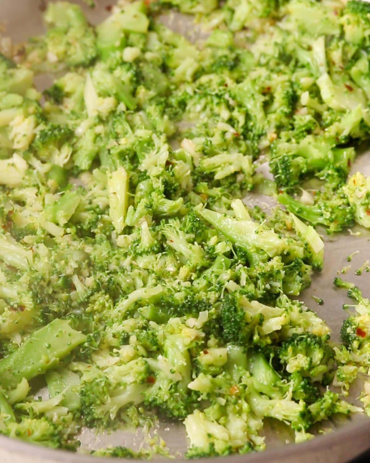 Mashed broccoli sizzling in a pan.