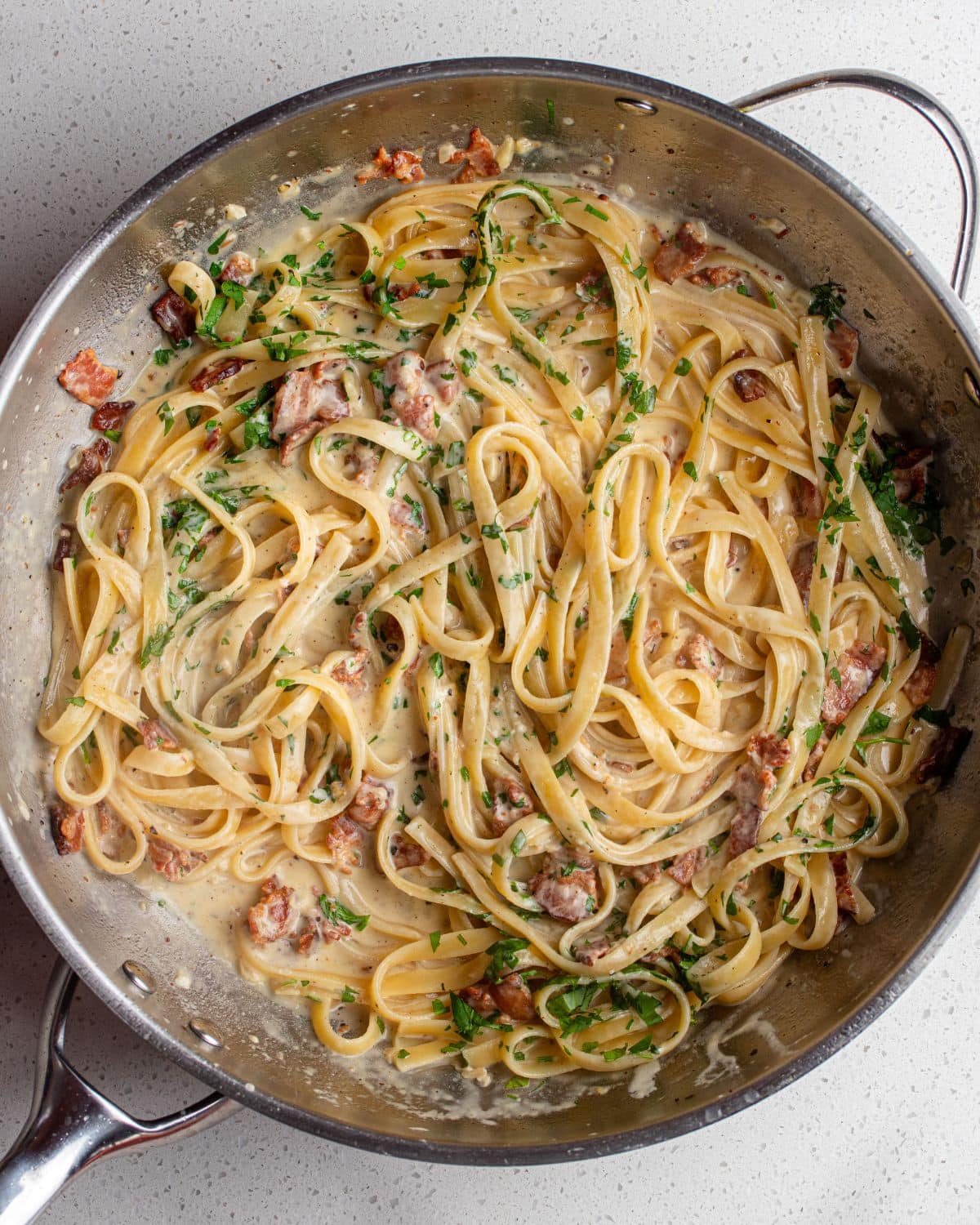 Fettuccine in a creamy bacon sauce in a stainless steel fry pan.