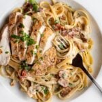 White plate with fettuccine pasta in a creamy bacon and chicken sauce. Fork resting in.