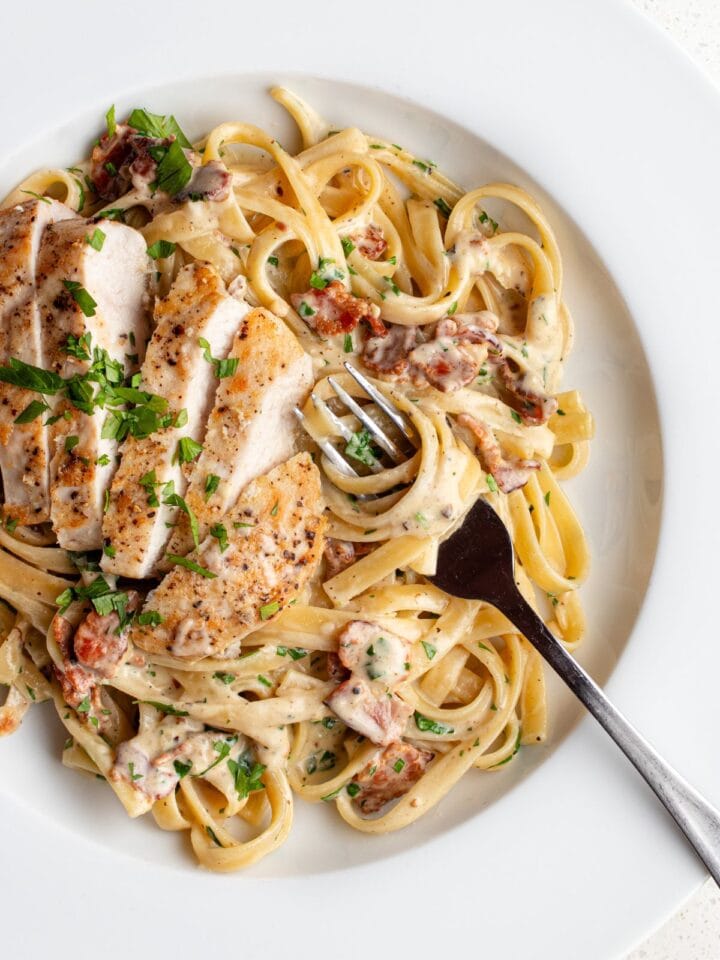 White plate with fettuccine pasta in a creamy chicken bacon sauce. Fork resting into pasta.