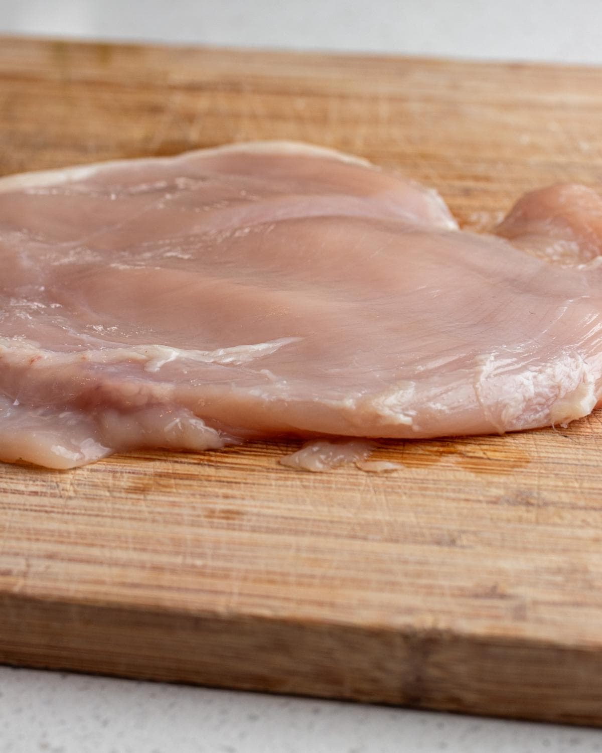 Chicken breast on a wooden cutting board.