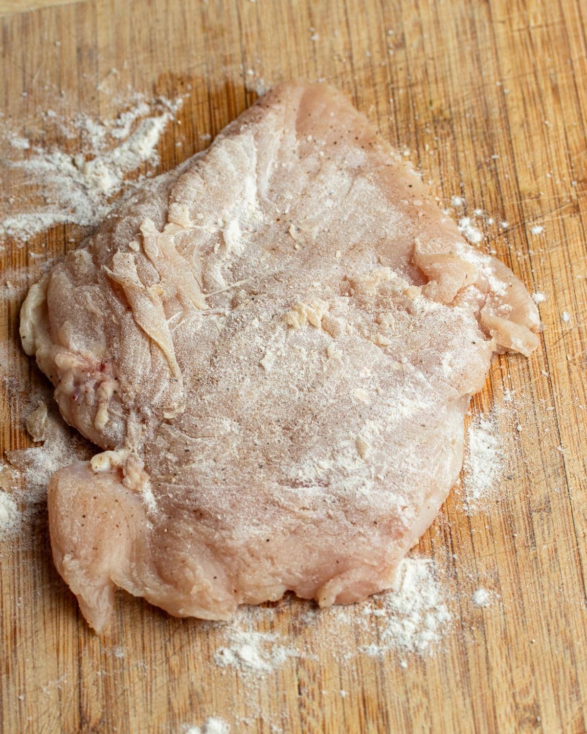 Chicken breast on a wooden cutting board dusted with flour.