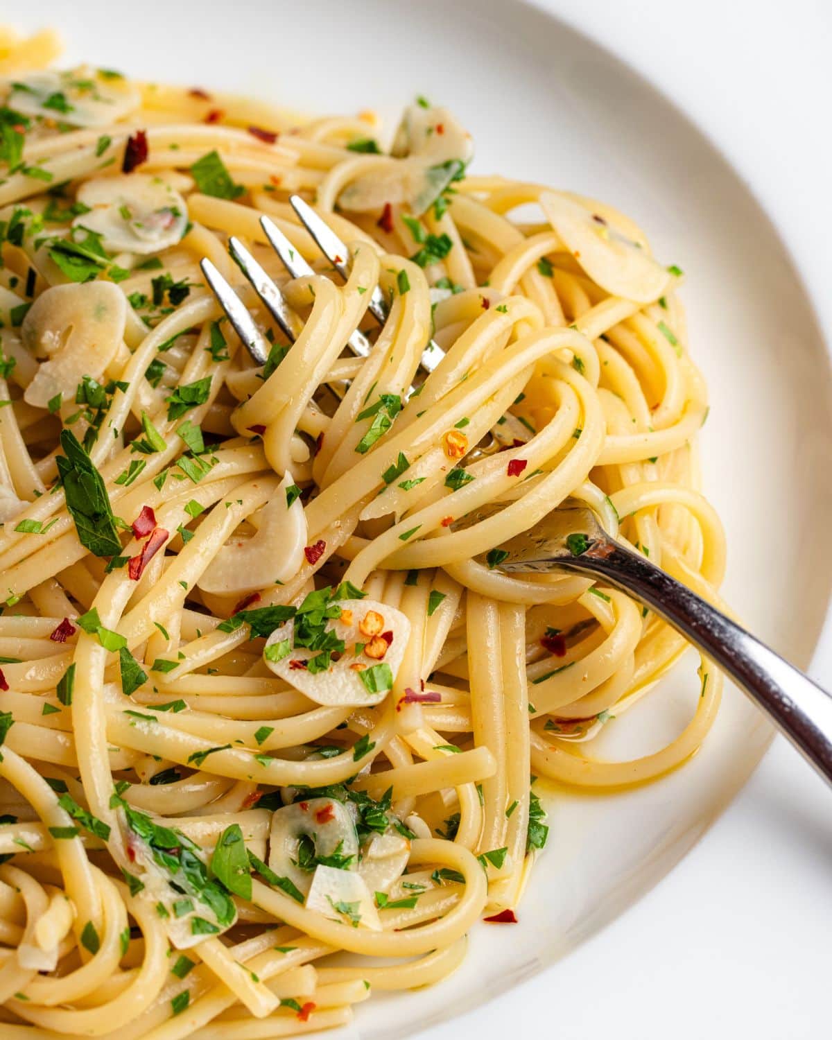Noodles wrapped around a fork with parsley, chilli flakes and garlic.