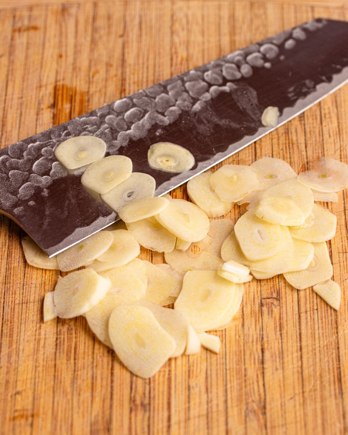 Sliced garlic on a wooden cutting board with a knife resting.