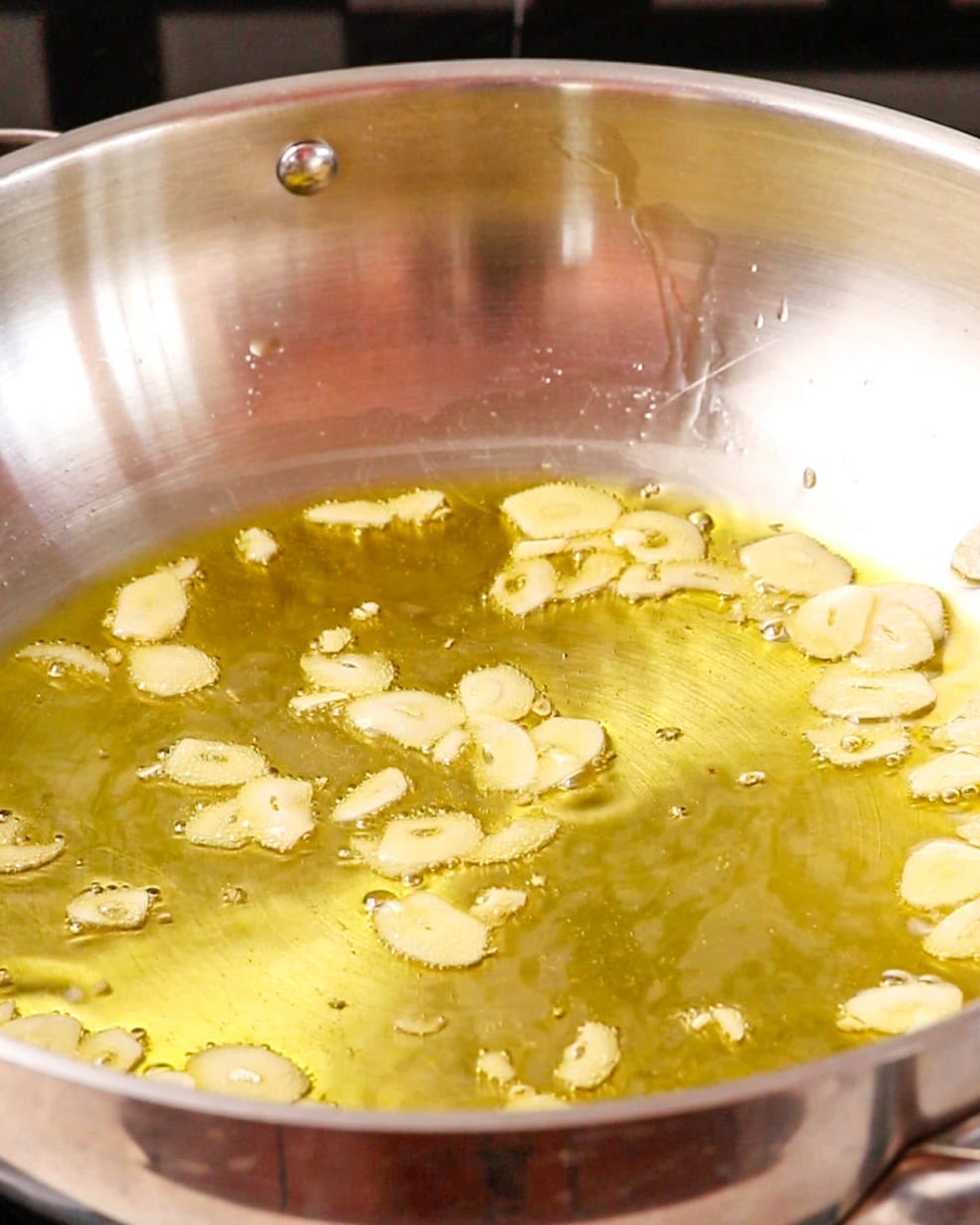 Sliced garlic and olive oil sizzling in a pan.