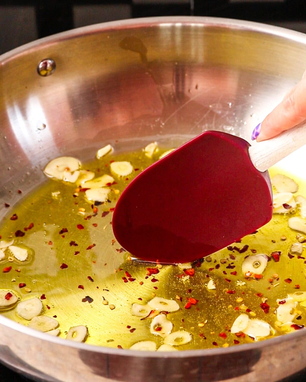 Chilli flakes added and a spatula mixing with garlic.