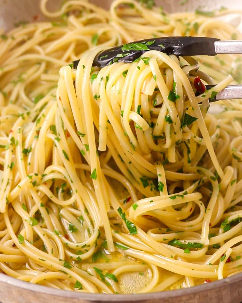 Tongs holding up the spaghetti with parsley mixed through.