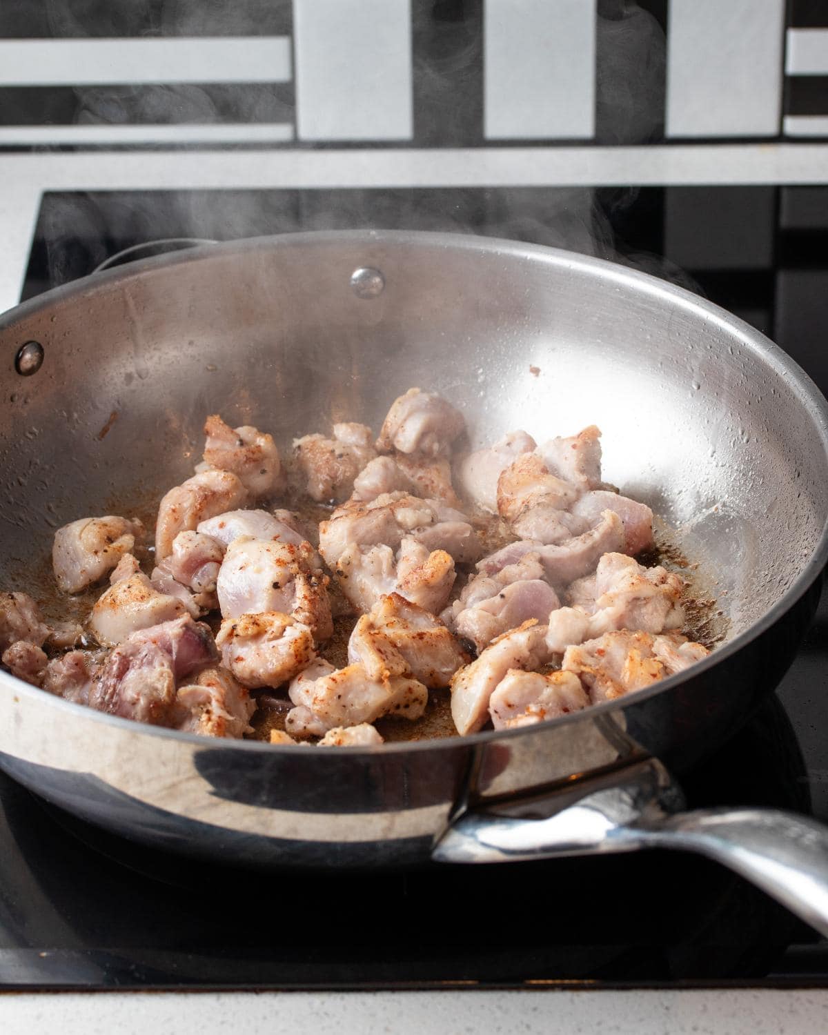 Chicken pieces sizzling in a stainless steel pan. 