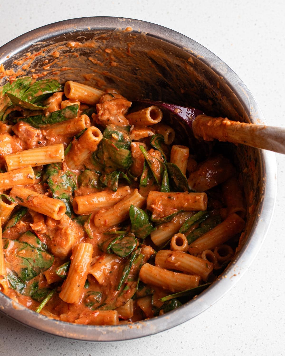 Cooked pasta and spinach mixed into the sauce in a mixing bowl.