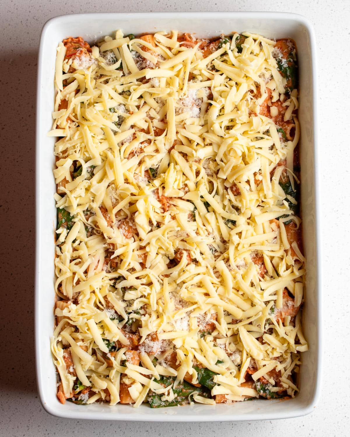 Cheese sprinkled on top of pasta mixture in the dish.