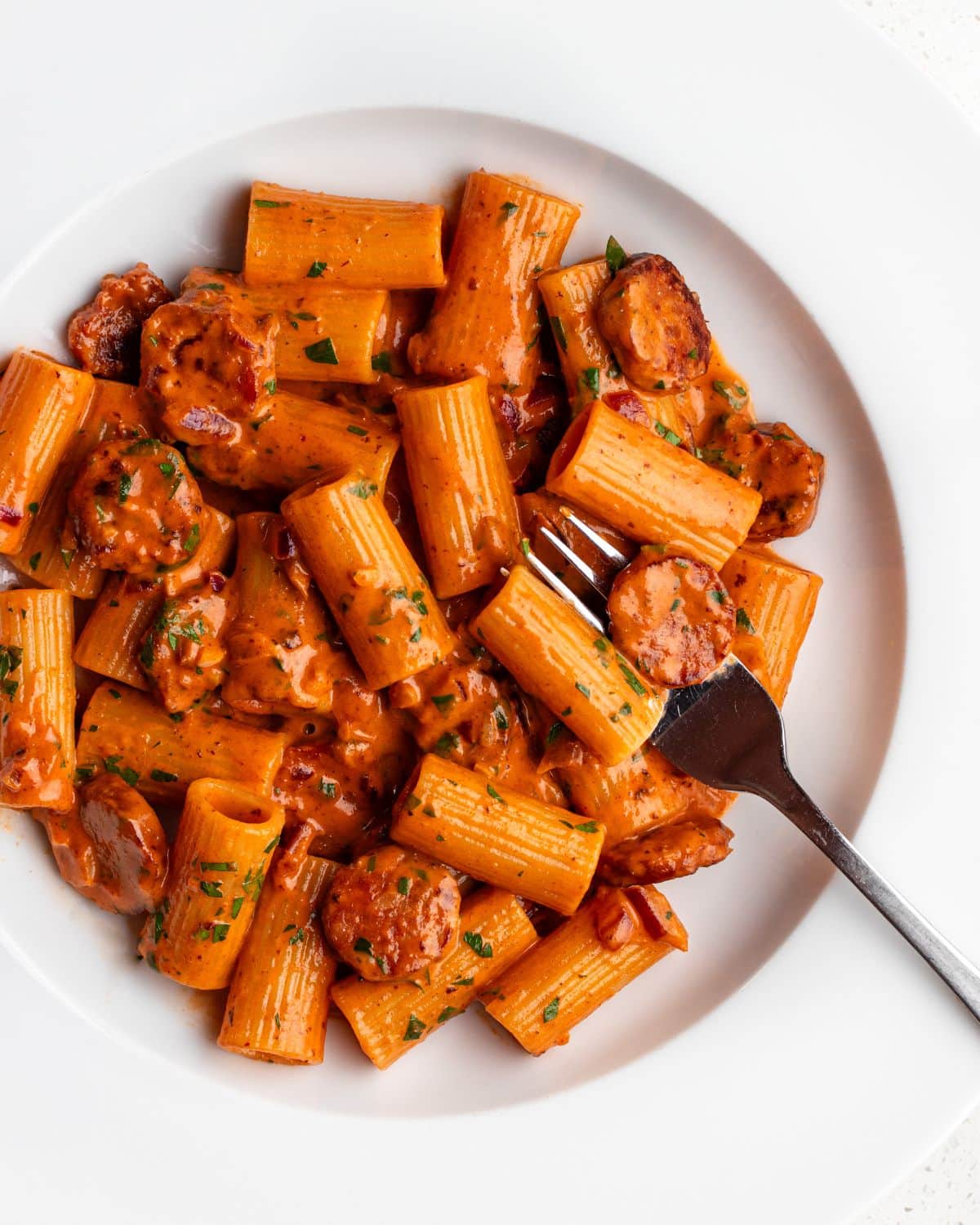 White plate with rigatoni pasta in a creamy chorizo sauce. Fork resting in.