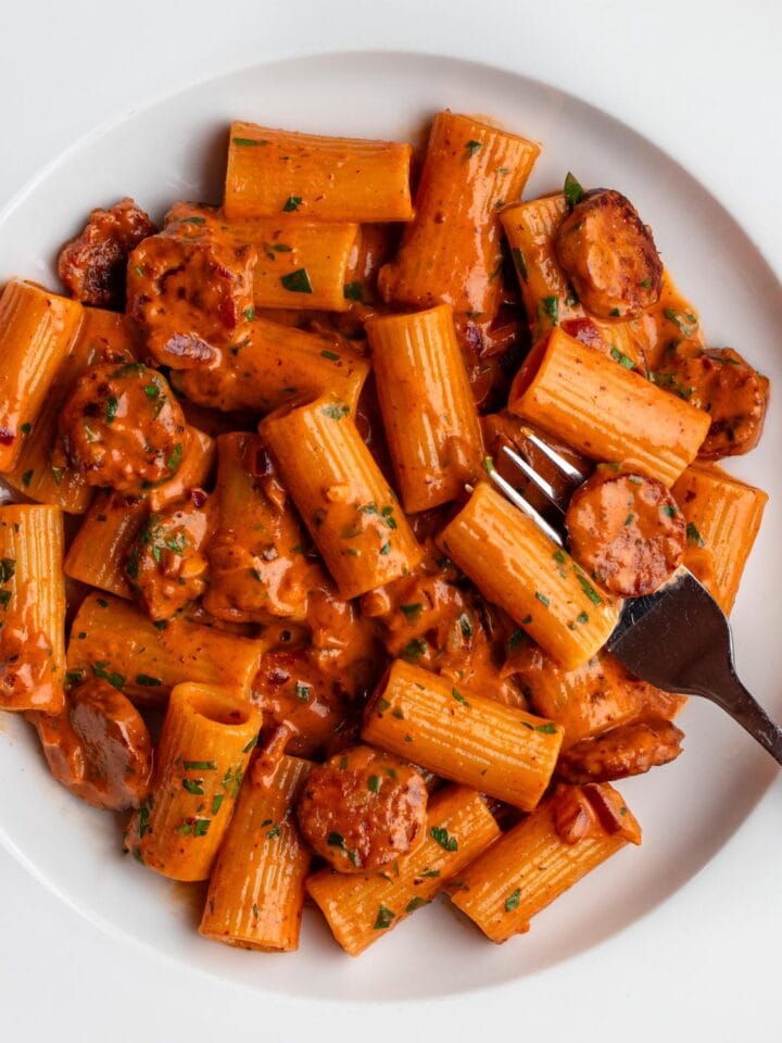 White plate with rigatoni pasta in a creamy chorizo sauce. Fork resting in.