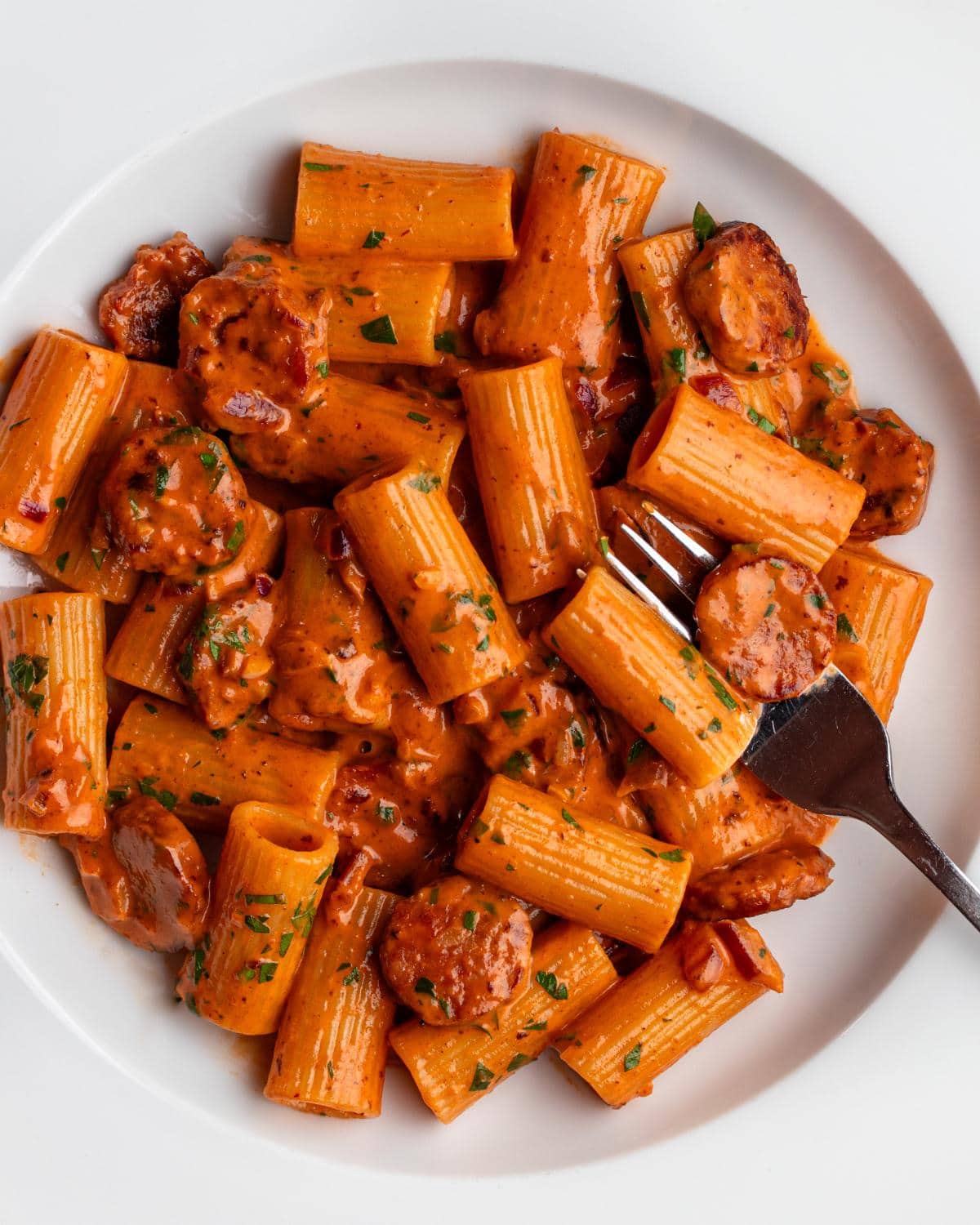 White plate with rigatoni pasta in a creamy chorizo sauce. Fork resting in.