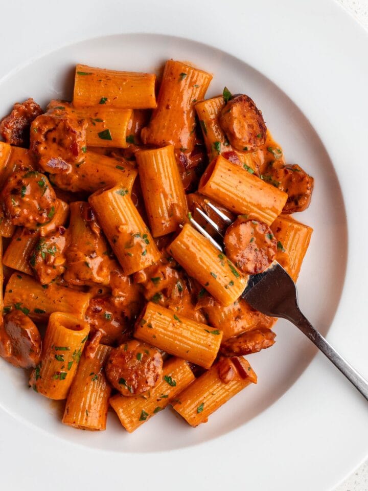 White plate with rigatoni pasta in a creamy chorizo sauce. Fork resting in.