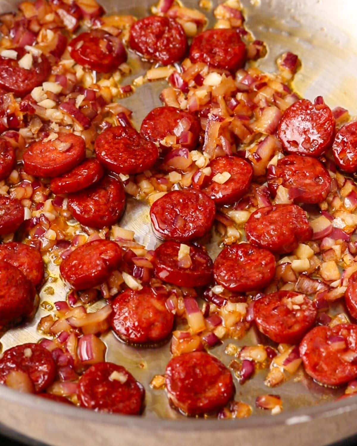 Onion and garlic sizzling with the chorizo in a pan.