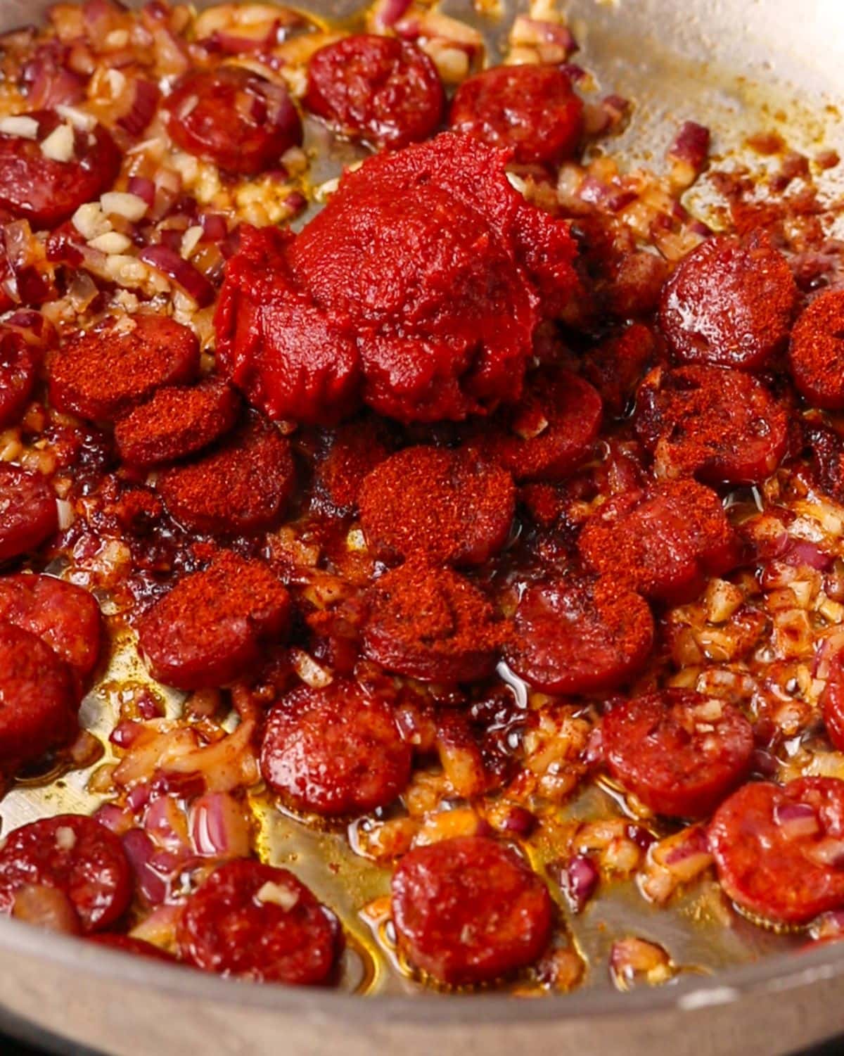 Paprika and tomato paste sitting on top of onion and sausage mixture.