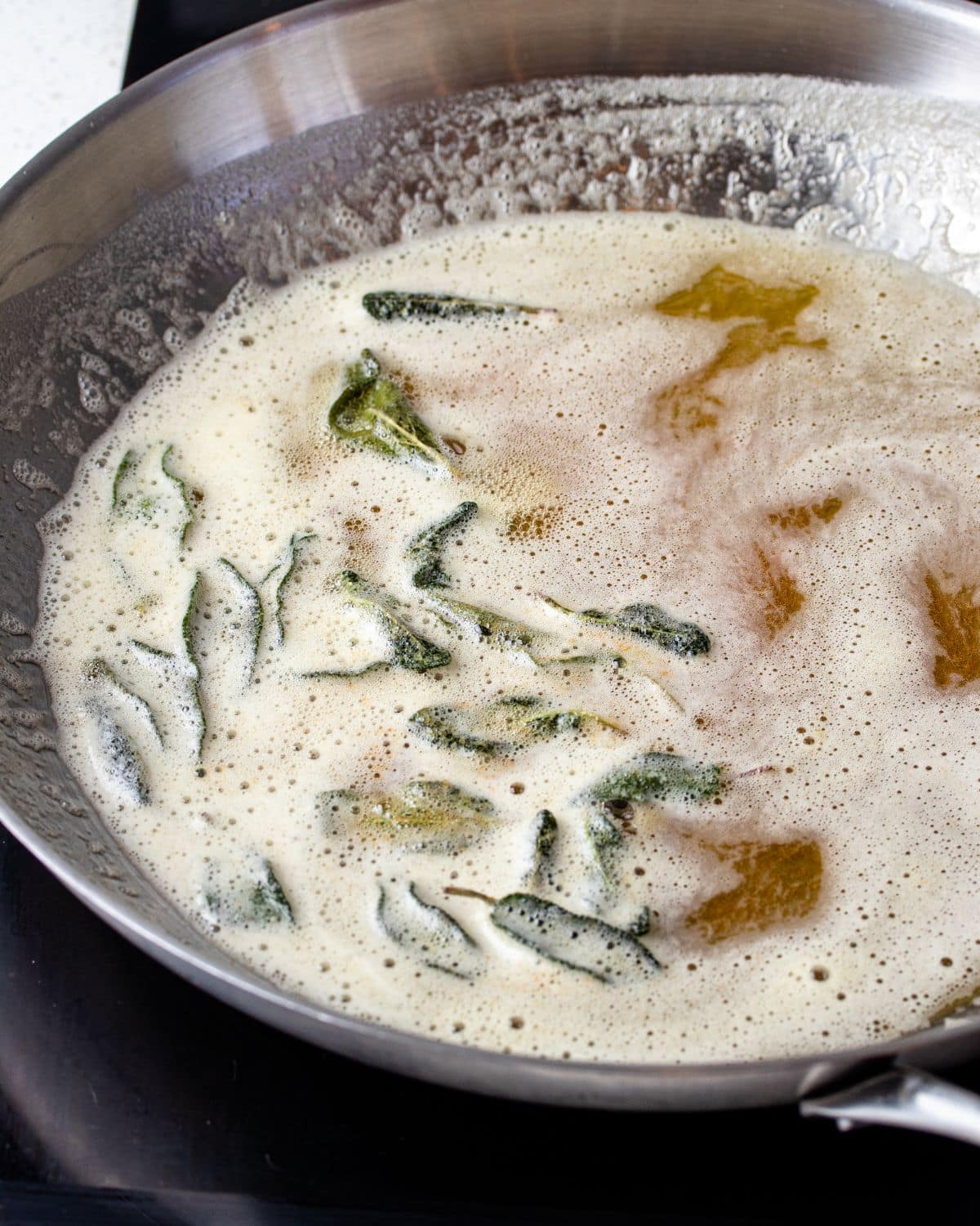 Browned foamy butter and crisp sage leaves in a stainless steel pan.