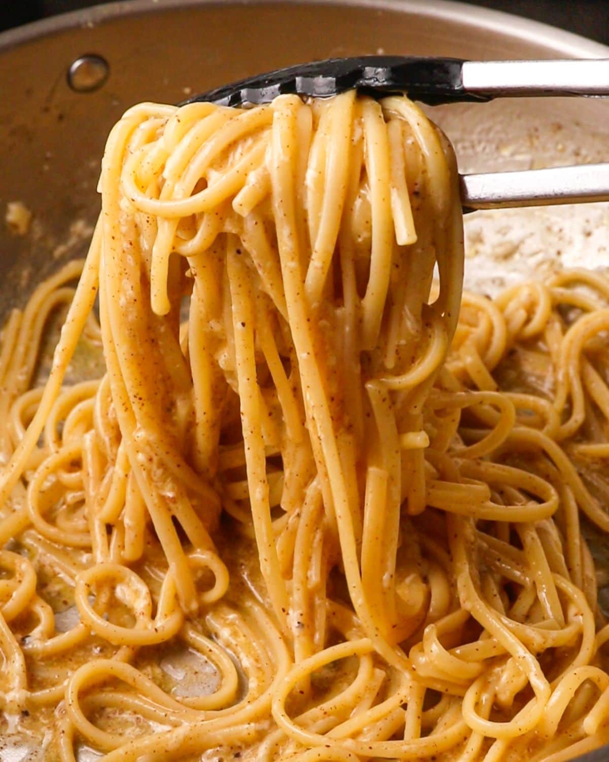 Tongs lifting up the pasta with a glossy sauce.