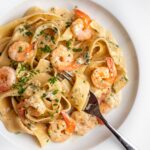White plate with pappardelle pasta in a creamy shrimp pasta sauce. Fork resting in with noodles wrapped around it.