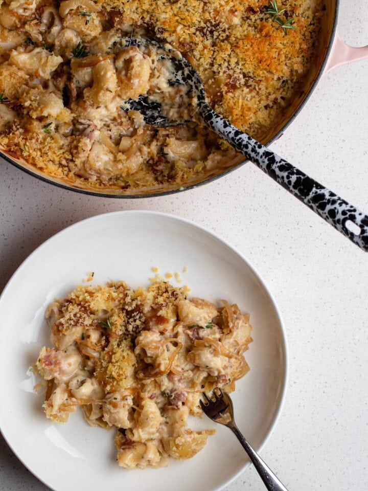 A plate with french onion mac and cheese and the casserole dish above with remaining pasta and serving spoon.