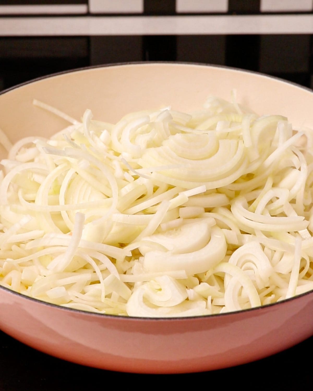 Raw sliced onions in a cassrole dish on a stove top.