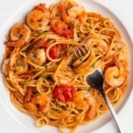 Spaghetti in a garlic butter shrimp sauce with cherry tomatoes and a fork resting onto the white plate.