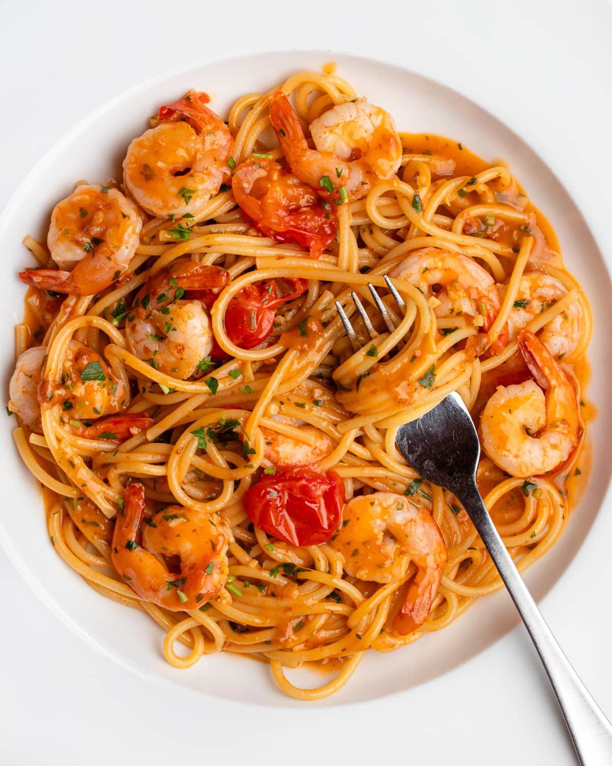 Spaghetti in a garlic butter shrimp sauce with cherry tomatoes and a fork resting onto the white plate.