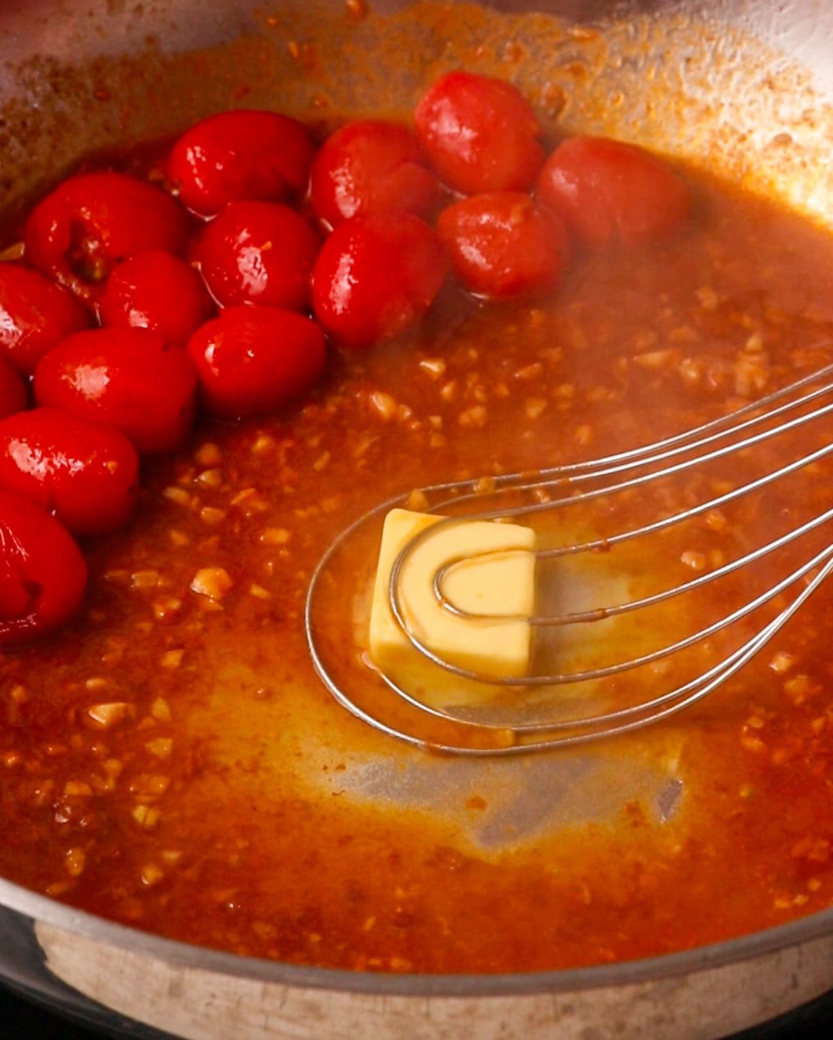 A cube of butter being whisked into the wine mixture with a whisk.