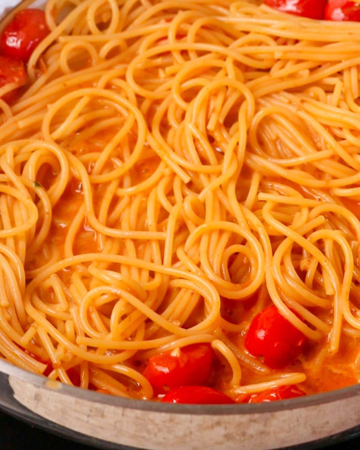 Cooked spaghetti added into the sauce in the fry pan.