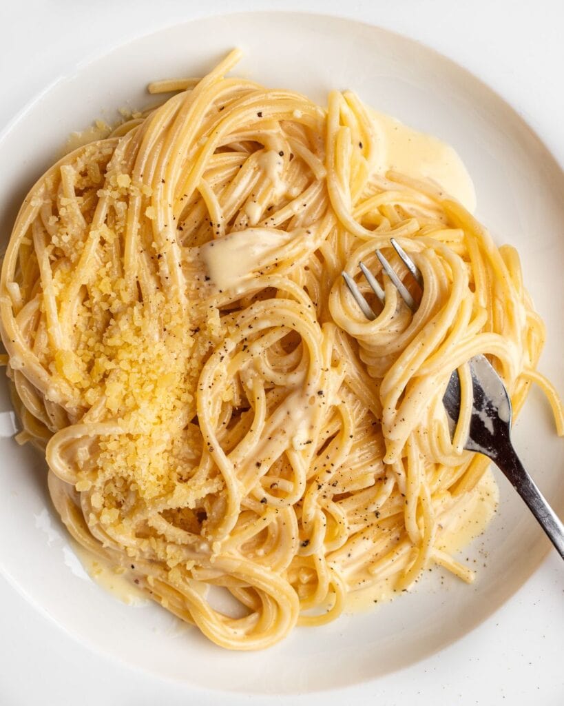 A white plate with spaghetti in a creamy white pasta sauce. A fork resting with noodles wrapped around it.