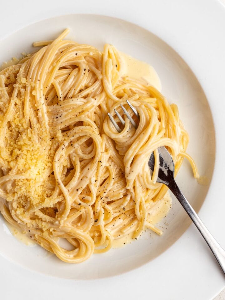 A white plate with spaghetti in a creamy white pasta sauce. A fork resting with noodles wrapped around it.
