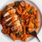 White plate with fusilli pasta in a creamy chorizo sauce with sliced chicken on top.