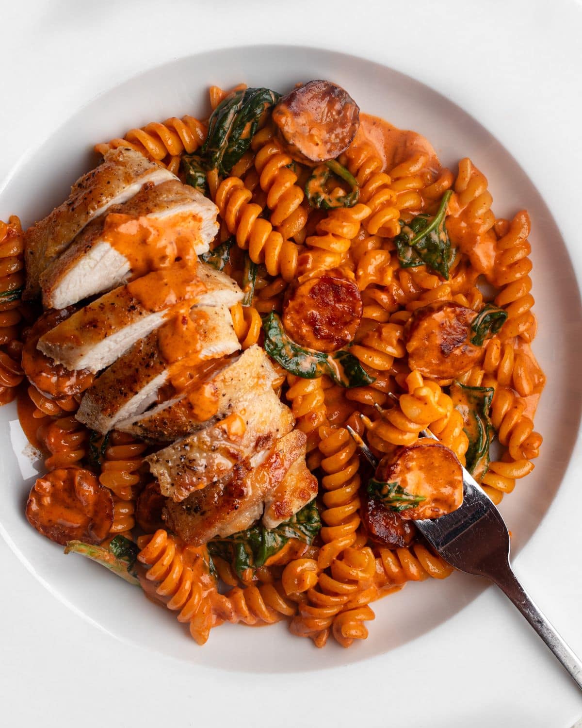 White plate with fusilli pasta in a creamy chorizo sauce with sliced chicken on top.