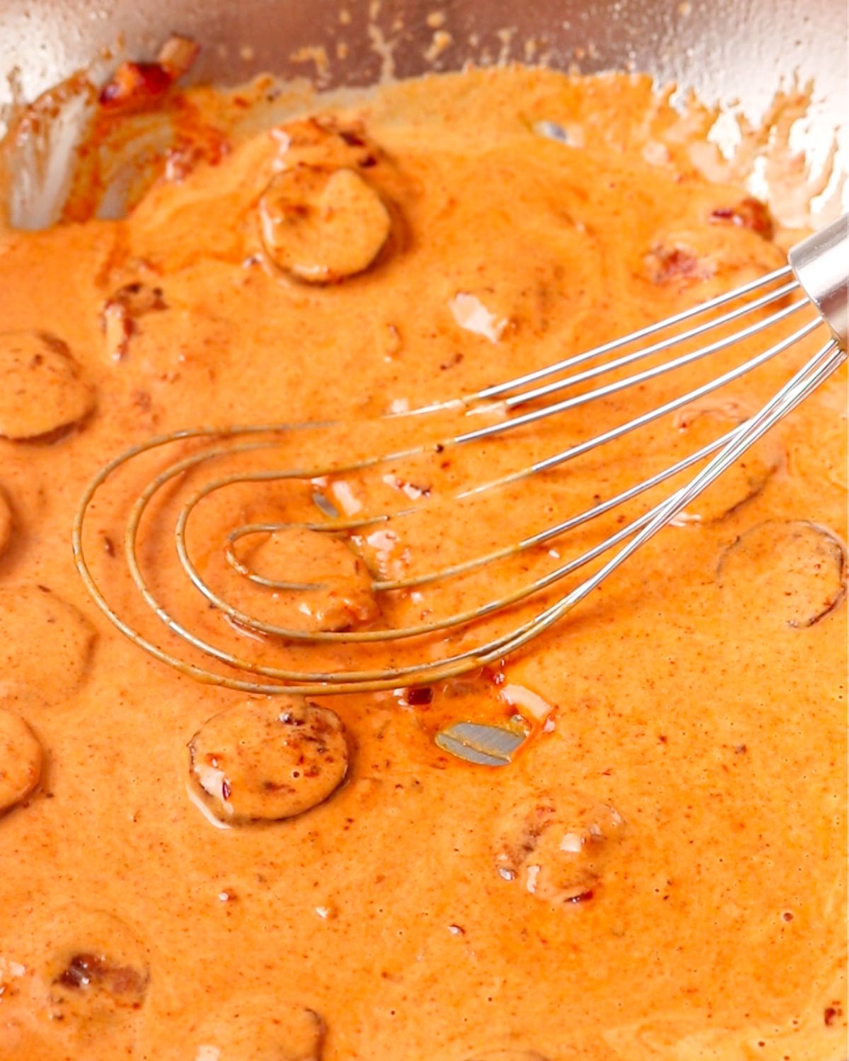 A whisk mixing cream into pan creating a smooth orange colored sauce.