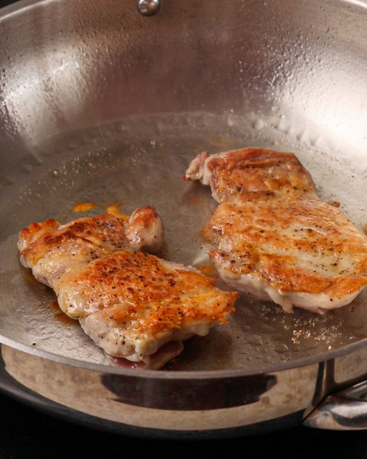 Golden crusted chicken thighs sizzling in a stainless steel pan.