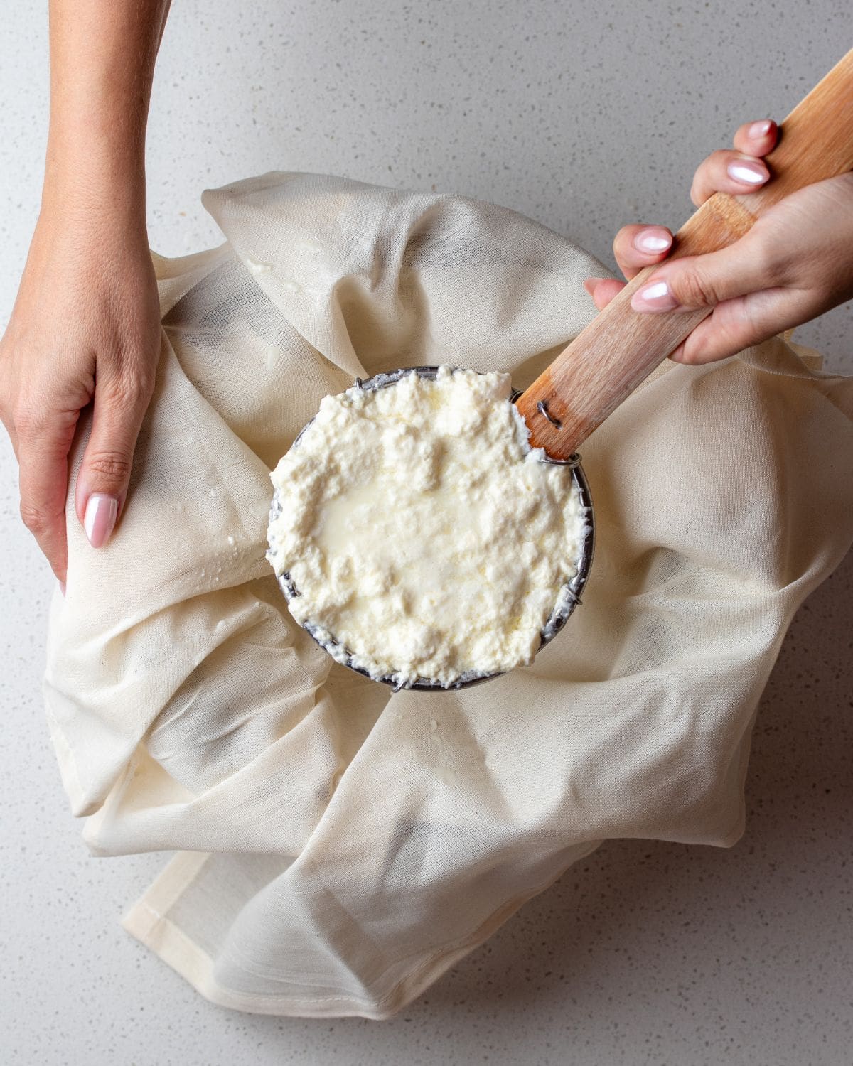 A strainer holding up homemade ricotta above a bowl lined with cheesecloth.