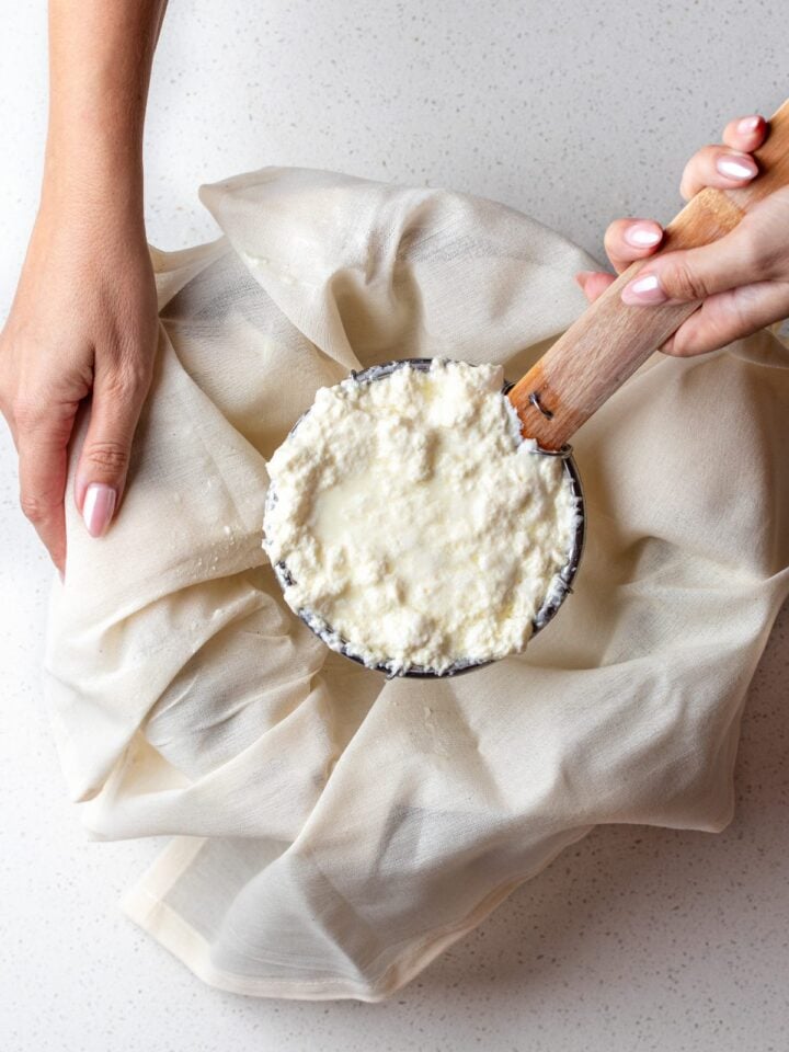 A strainer holding up homemade ricotta above a bowl lined with cheesecloth.