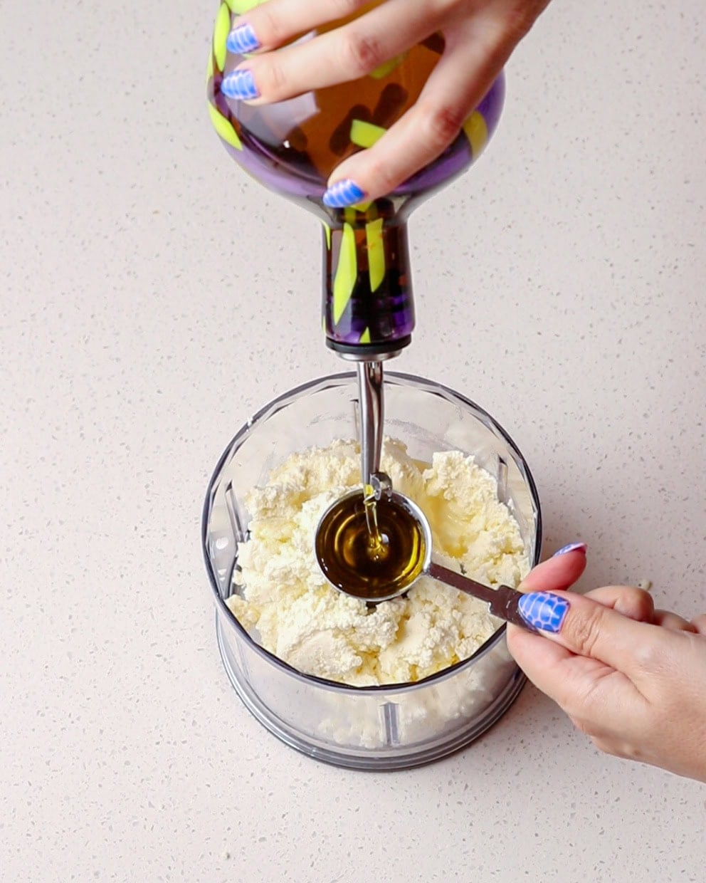 Olive oil being poured on top of ricotta in a blender.