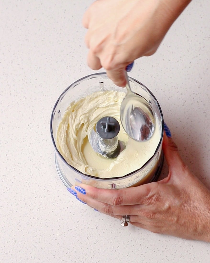 Smooth whipped ricotta cheese being spread with a spoon in blender.