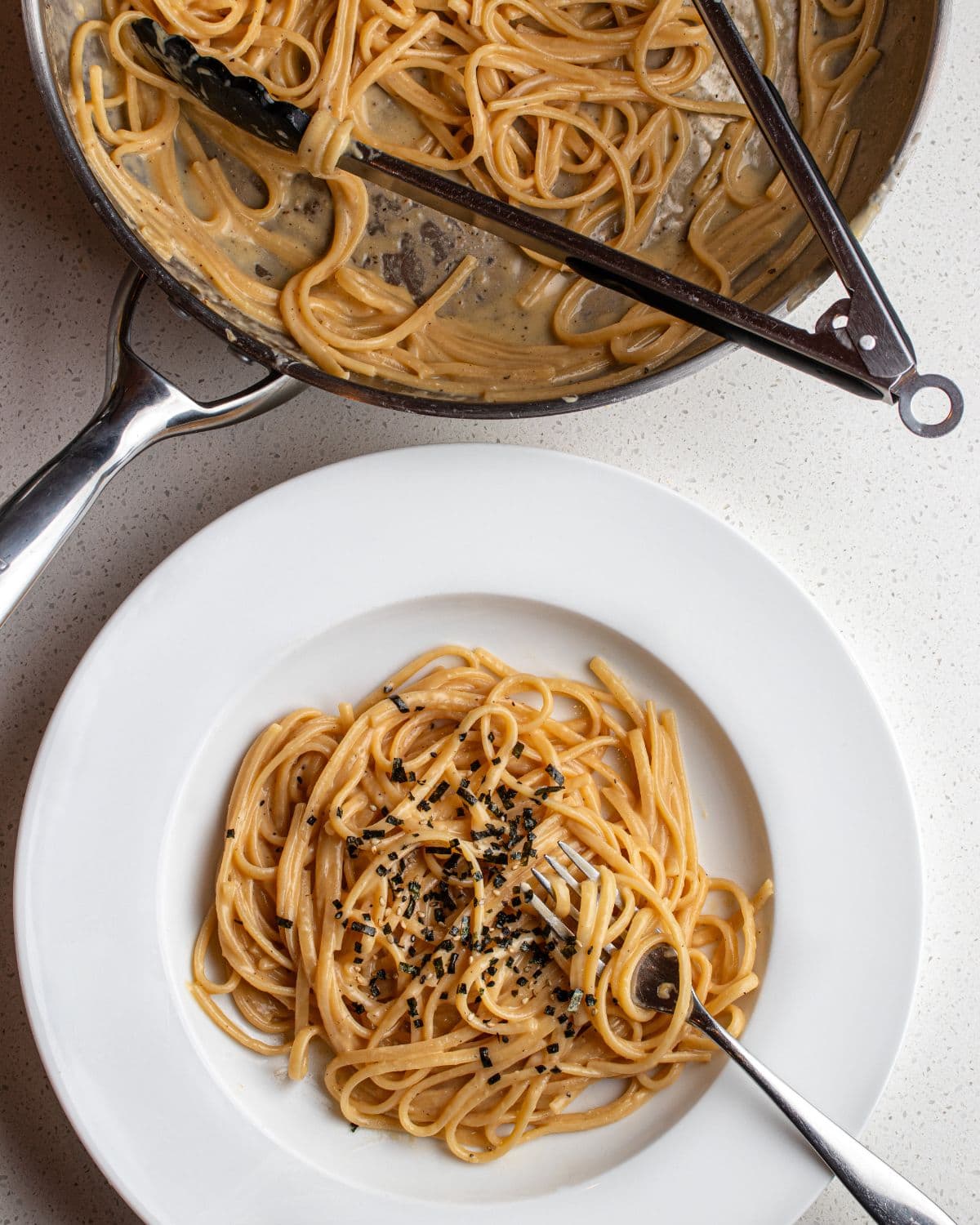 White plate with miso butter pasta and a fork twirling the spaghetti. Above is the pan with remaining pasta and tongs.