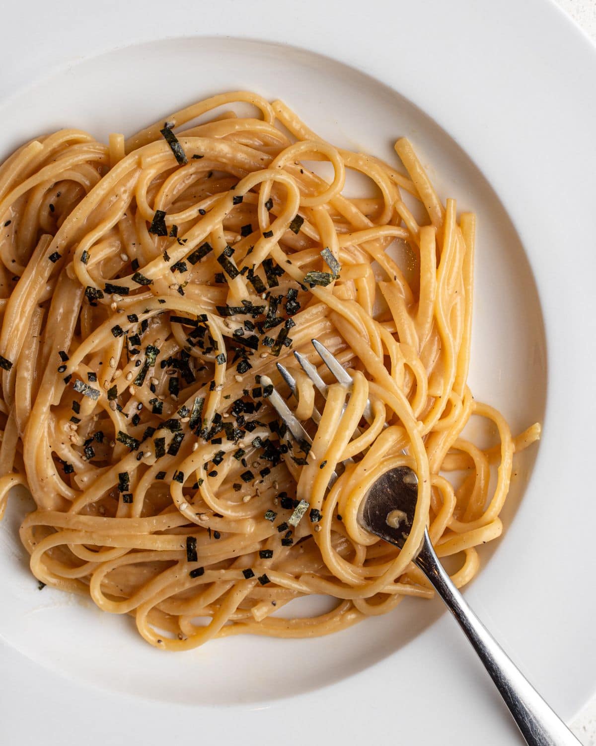 White plate with spaghetti in a miso butter sauce. Furikake sprinkled on top.