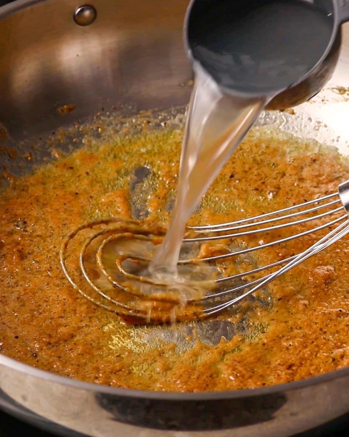Pasta water being poured into the pan with a whisk laying.