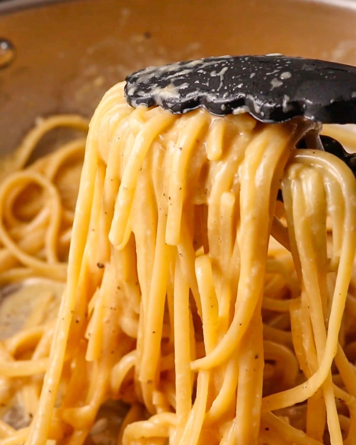 Tongs holding up the strands of pasta coated in the miso butter sauce.