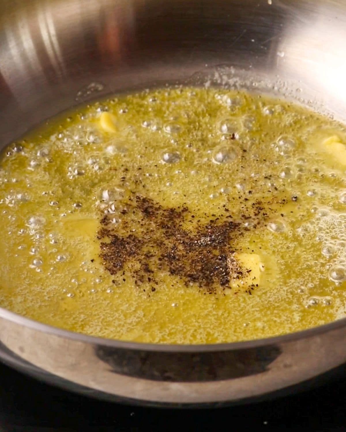 Butter and pepper sizzling in a stainless steel fry pan.