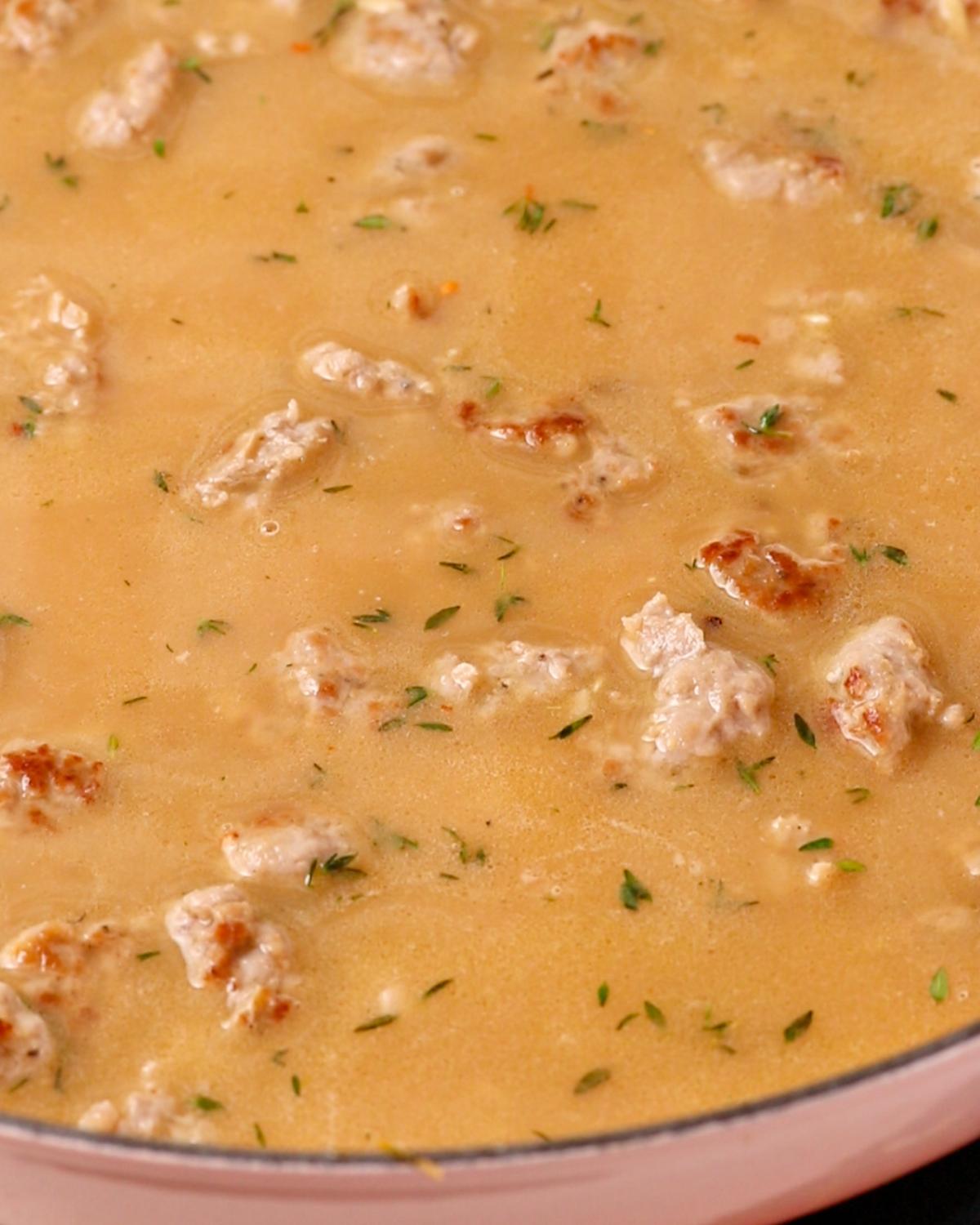 Chicken stock added into pan with bits of sausage poking out at top.