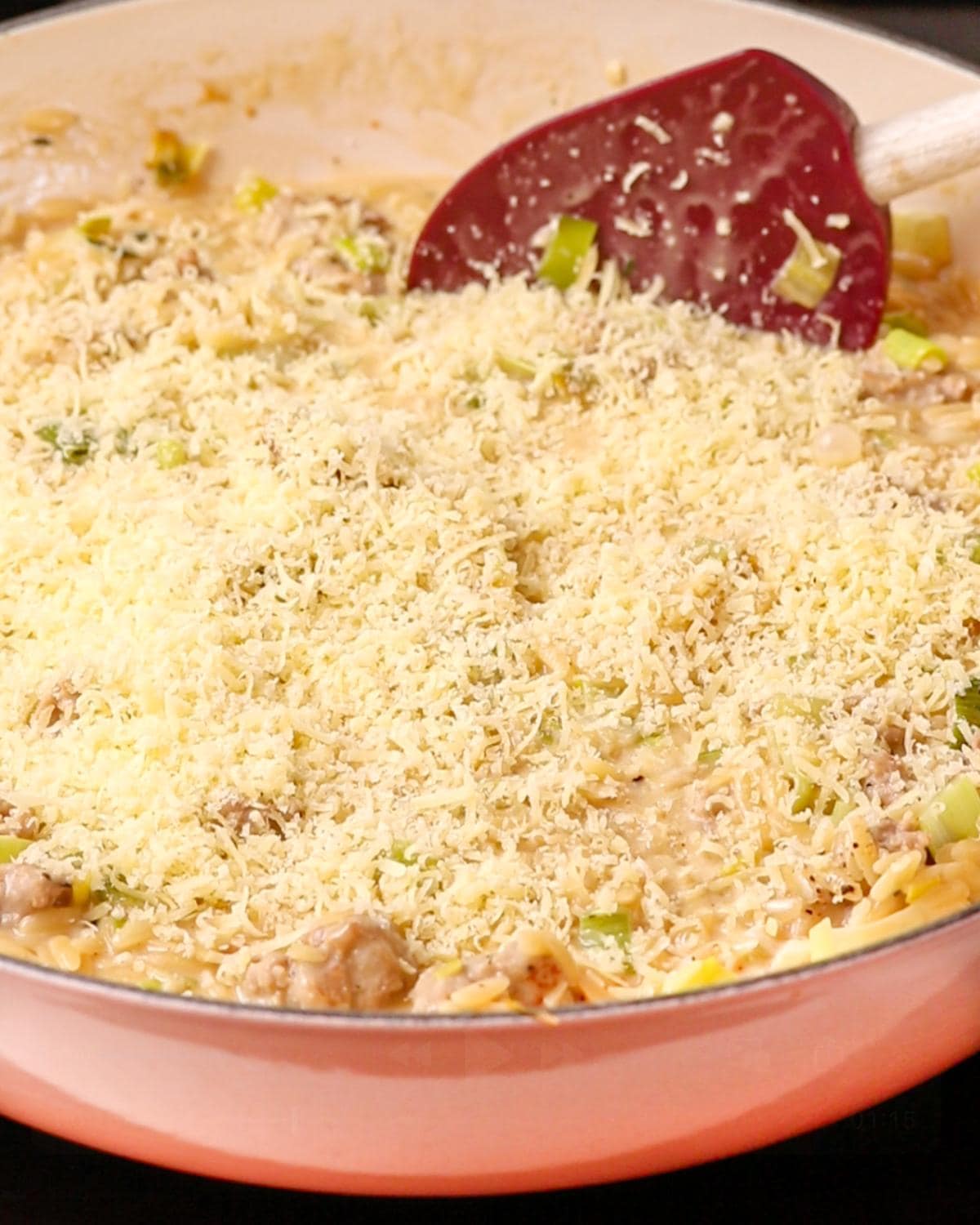 Grated parmesan on top of orzo with spatula resting in.