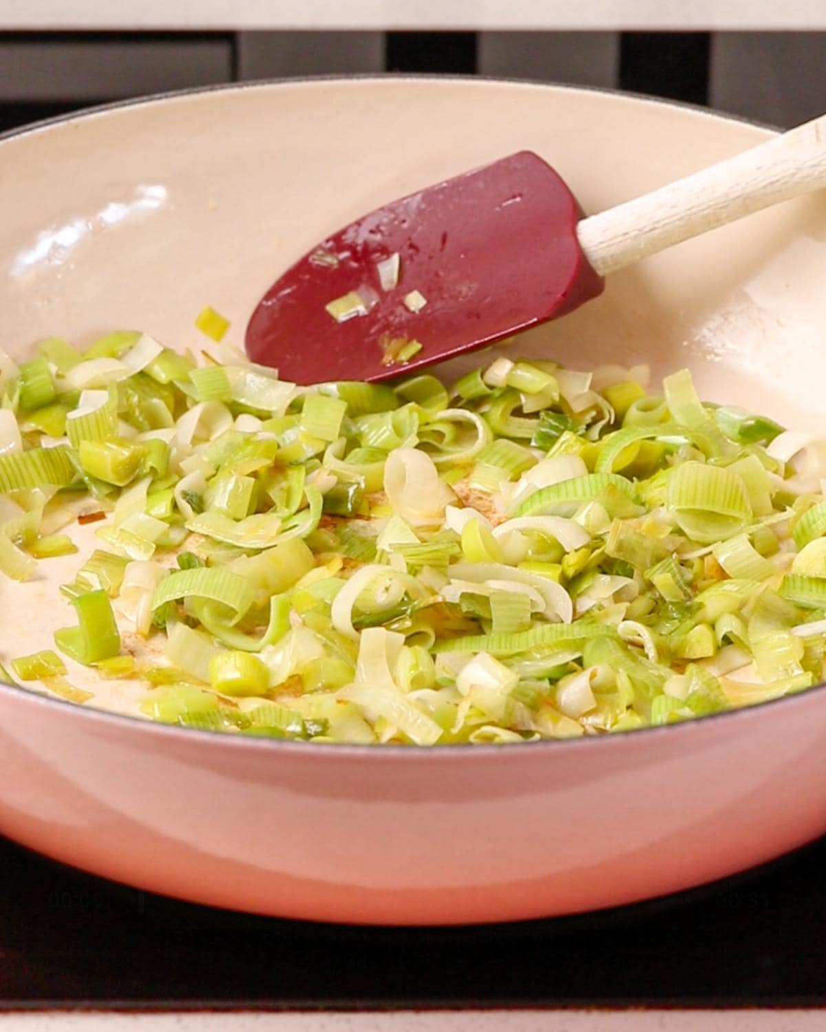 Sliced leeks cooking in a casserole dish on a stovetop.