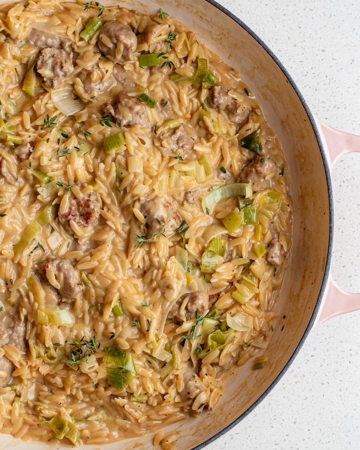 Creamy orzo with sausage pieces and leeks mixed through. In a round casserole pot.